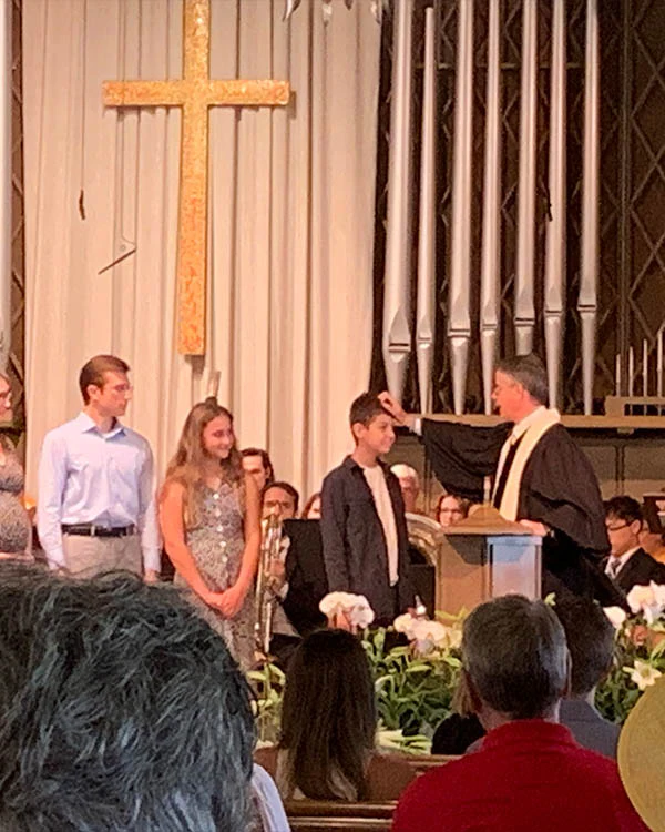 Kid being baptized next to his parents
